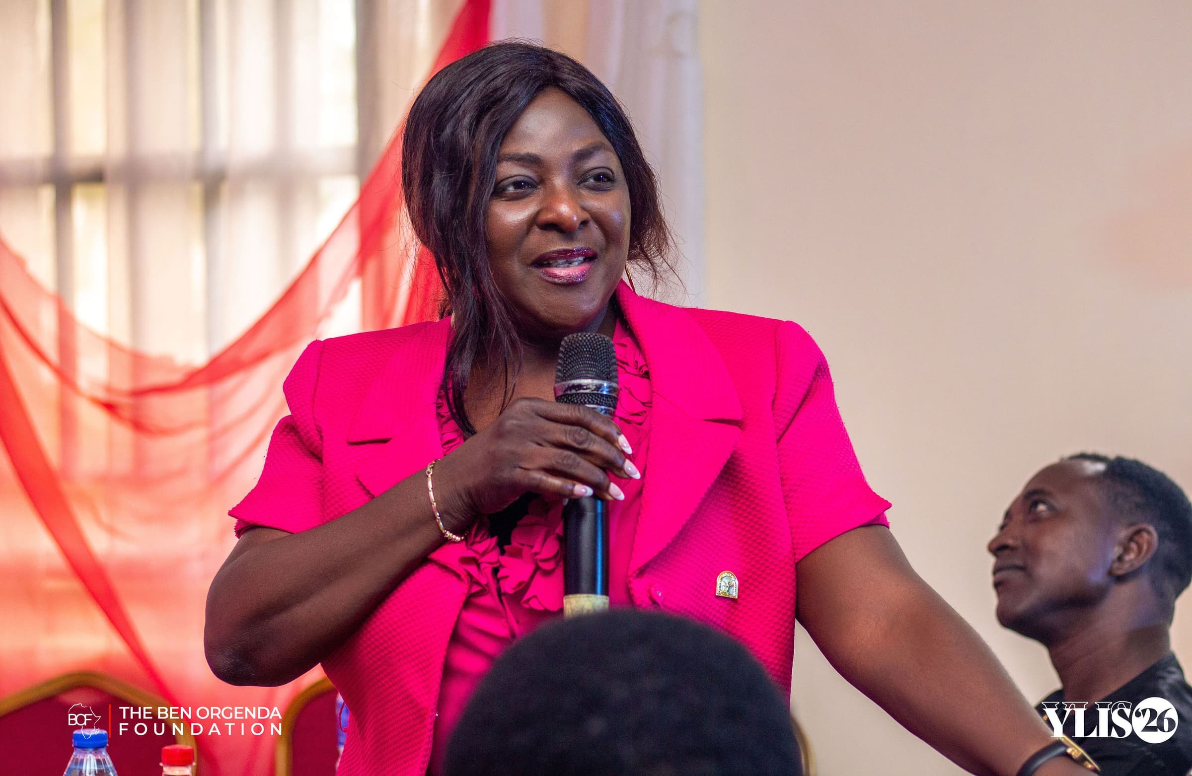 A speaker in a pink blazer addressing the audience